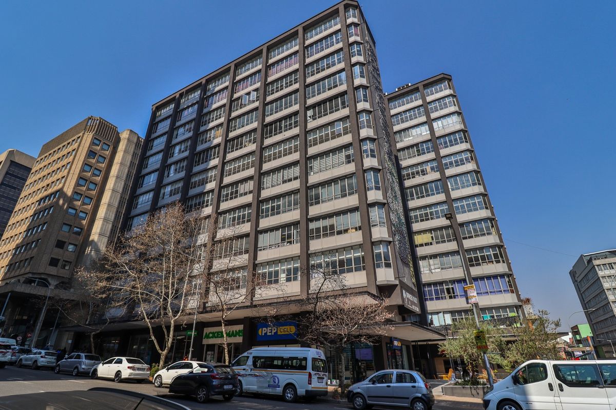 A multi-story commercial building featuring a prominent facade with extensive glass windows and ground-level retail storefronts in an urban setting.