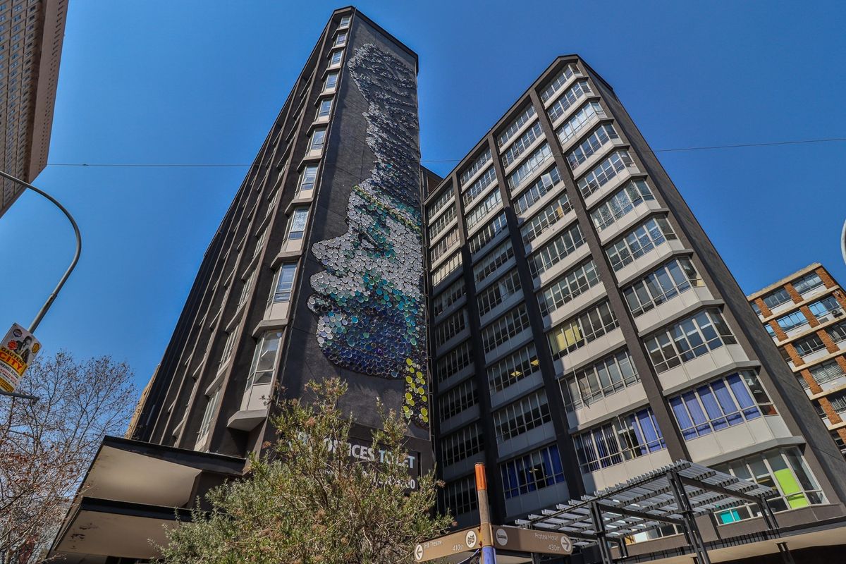 A low-angle view of a multi-story commercial building featuring a prominent artistic mural on the facade and extensive window glazing.