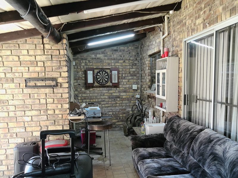 A covered patio area featuring exposed brick walls, timber rafters, and tiled flooring, providing a functional outdoor entertainment space with sliding door access.