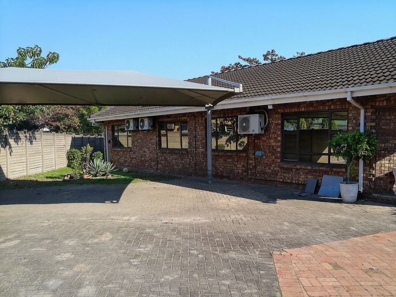 Exterior view of a brick-faced house featuring a paved driveway, a shade port, and multiple wall-mounted air conditioning units.