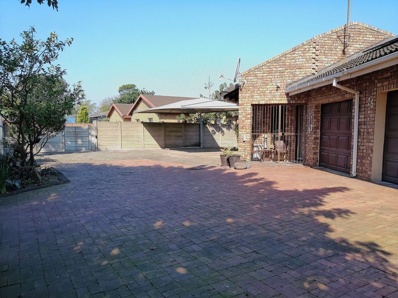 Front exterior view of the property featuring a paved driveway, brick facade, garage access, and a carport structure.