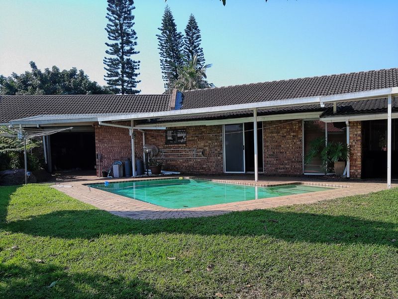 Rear exterior view featuring a swimming pool, brick paved surround, and a covered patio area attached to the main house structure.