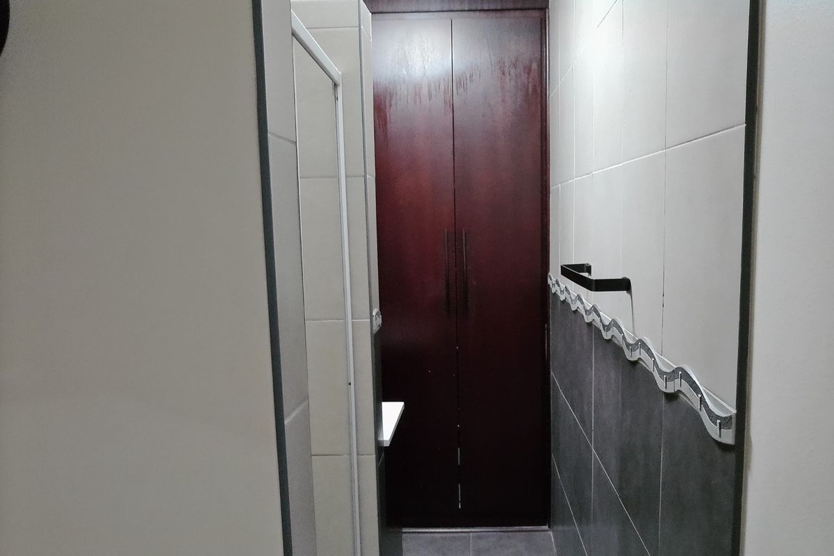 A compact bathroom featuring a shower enclosure, tiled walls with decorative border, and a built-in dark wood storage cupboard.