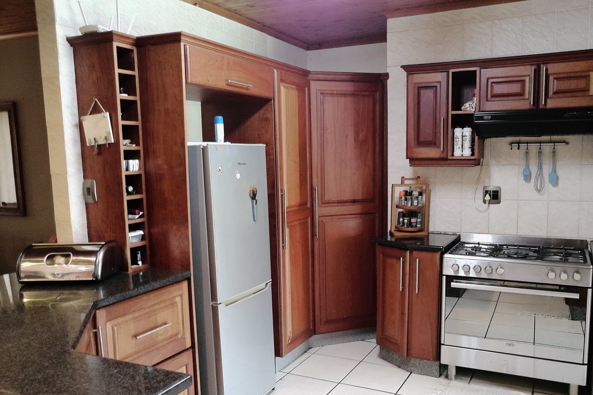 A functional kitchen featuring warm-toned wooden cabinetry, granite countertops, a gas stove with extractor fan, and tiled flooring.