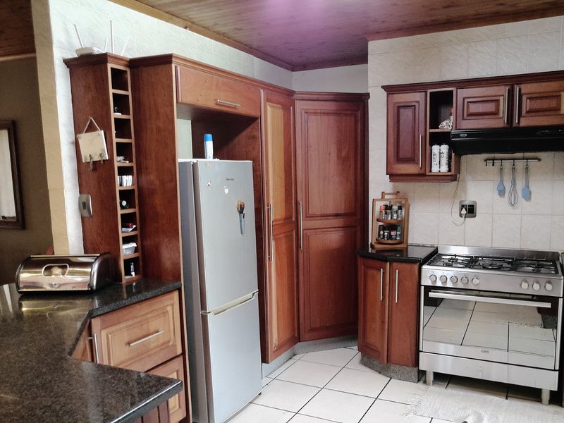 A functional kitchen featuring warm-toned wooden cabinetry, granite countertops, a gas stove with extractor fan, and tiled flooring.