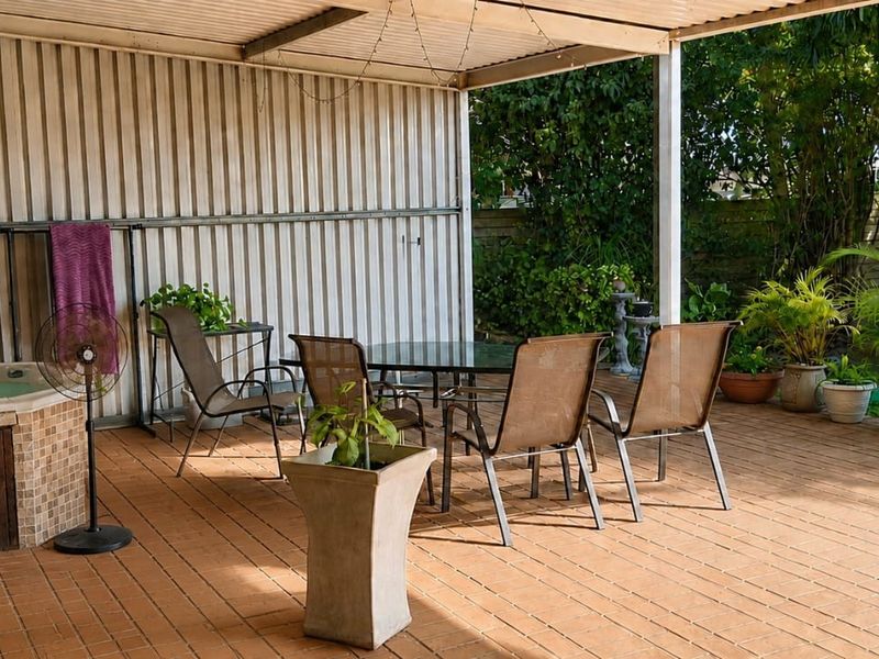 Covered outdoor patio area featuring a built-in spa, corrugated metal wall cladding, and tiled flooring, providing a functional space for outdoor relaxation.