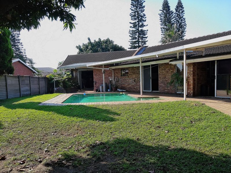 Rear view of the property featuring a swimming pool, a covered patio area, and a spacious garden with brick exterior walls.