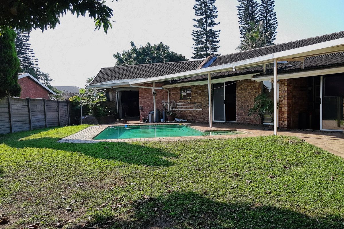 Rear view of the property featuring a swimming pool, a covered patio area, and a spacious garden with brick exterior walls.