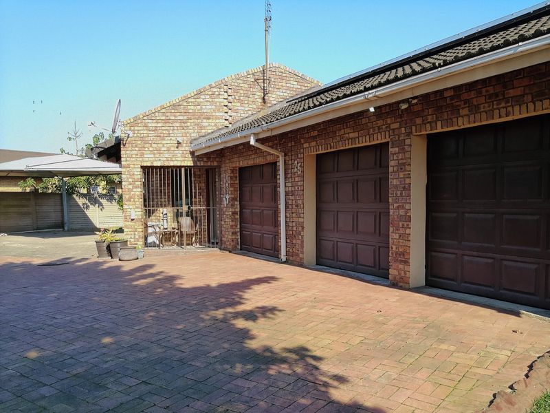Front exterior view of the property featuring a triple garage with brown sectional doors, brick facade, and a paved driveway.