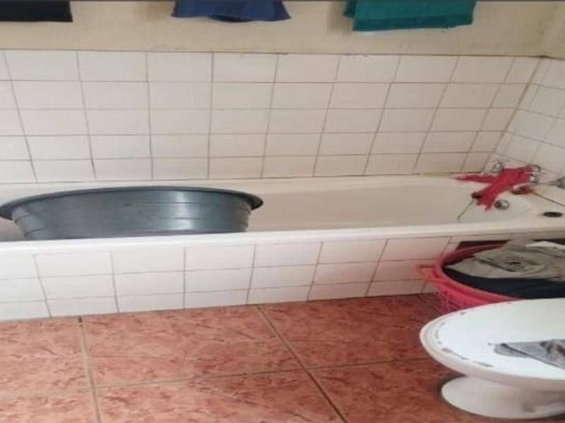 A dated bathroom featuring a built-in bathtub with tiled surround, ceramic floor tiles, and standard sanitaryware, requiring cosmetic updates to improve its condition.