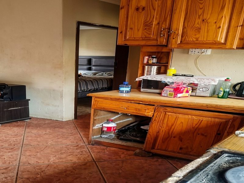 A kitchen area featuring wooden cabinetry and tiled flooring, currently showing significant wear and damage to the built-in storage units.