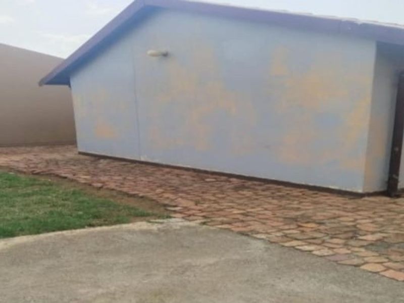Rear exterior view of the property showing a paved walkway, security bars on the window, and weathered exterior wall paint.