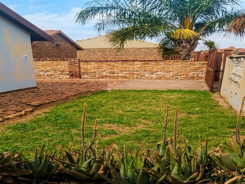 A rear garden area featuring a paved patio, concrete slab, and brick boundary wall, requiring maintenance to the exterior wall finish and balustrade.