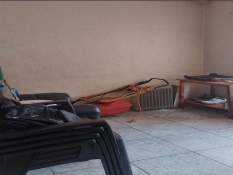 A living room area featuring tiled flooring and plain walls, currently used for storage and in need of cosmetic updates.