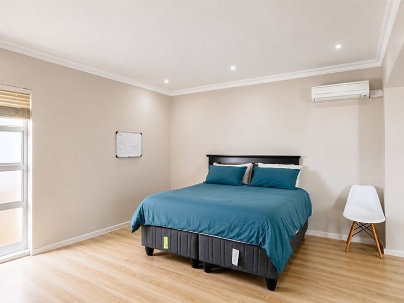 A well-maintained bedroom featuring light laminate flooring, recessed downlighting, and a wall-mounted split-system air conditioning unit.