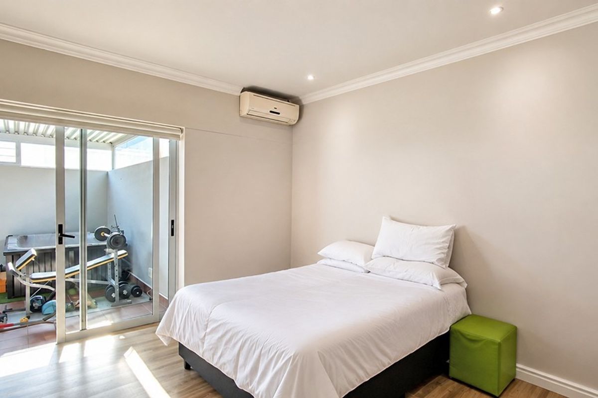 A well-maintained bedroom featuring laminate flooring, recessed lighting, and a wall-mounted air conditioning unit, with direct access to an outdoor patio area.