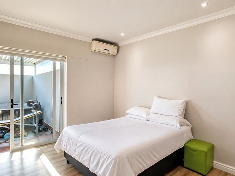 A well-maintained bedroom featuring laminate flooring, recessed lighting, and a wall-mounted air conditioning unit, with direct access to an outdoor patio area.