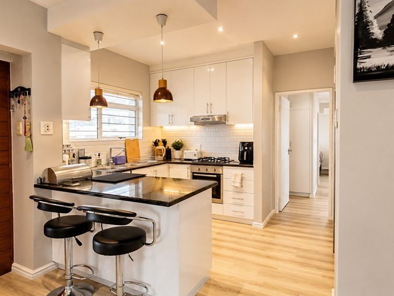 Modern kitchen featuring white cabinetry, granite countertops, subway tile backsplash, gas hob, and integrated appliances, complemented by warm pendant lighting and laminate flooring.
