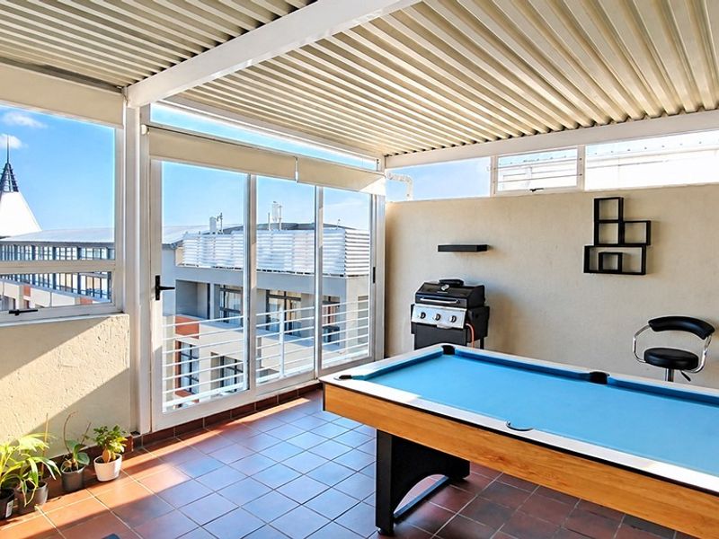 A covered balcony featuring tiled flooring, sliding glass doors, and a corrugated metal roof, offering an open-air space suitable for entertainment.