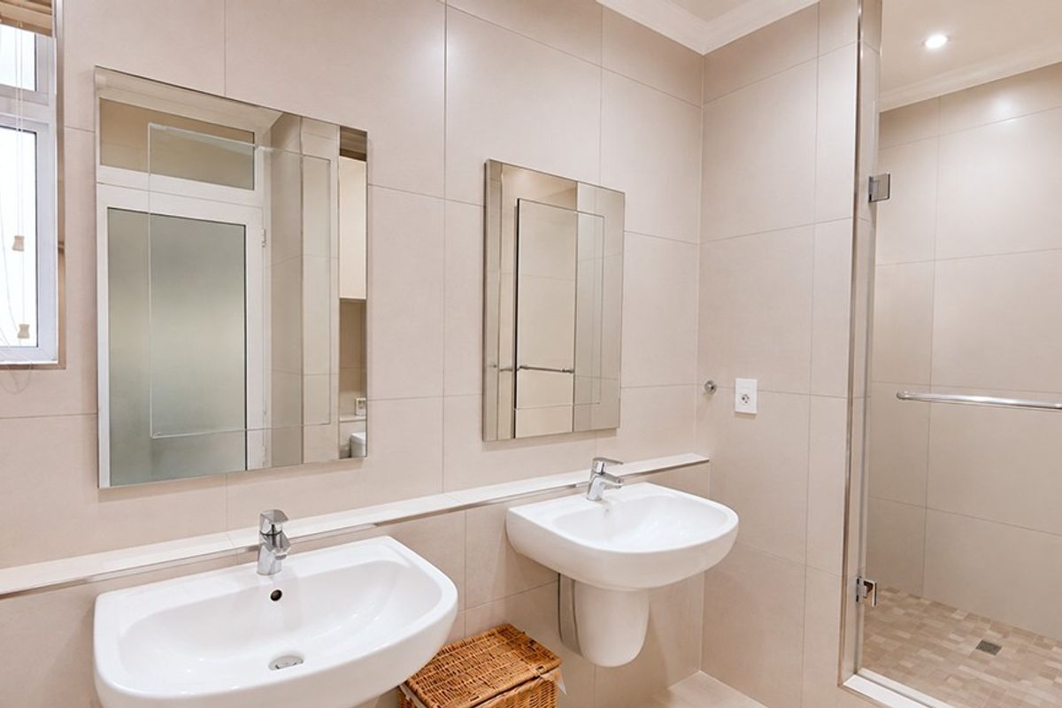 Modern bathroom featuring a double vanity with pedestal basins, wall-mounted mirrors, and a spacious glass-enclosed shower with neutral wall and floor tiling.