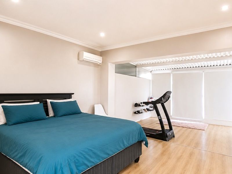 Spacious bedroom featuring light laminate flooring, recessed downlighting, and a wall-mounted split-system air conditioner, with an adjoining flexible space.