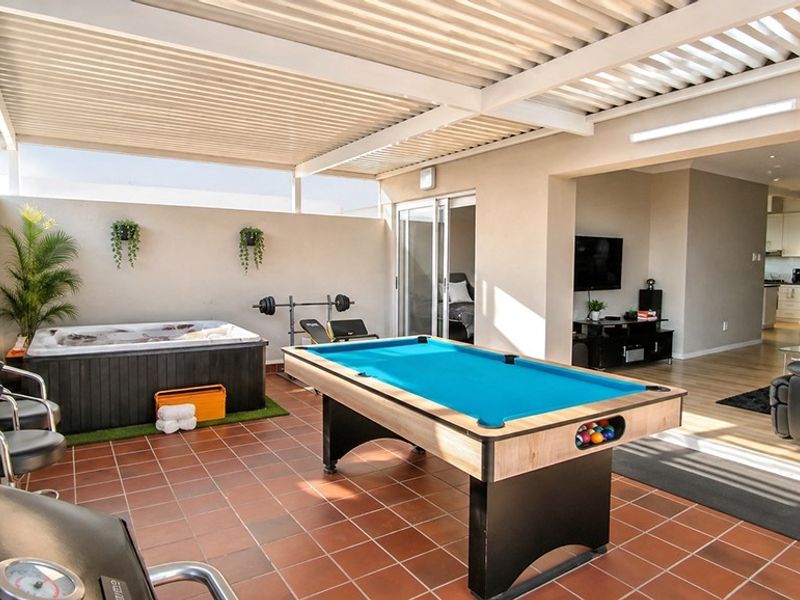 Spacious covered patio featuring terracotta tiling, recessed lighting, and seamless flow into the open-plan living area through large sliding glass doors.