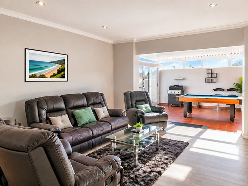 Spacious open-plan living area featuring laminate flooring, recessed lighting, and seamless transition to a covered tiled patio area.