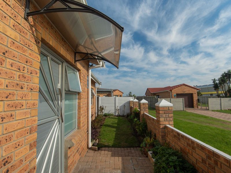 A well-maintained rear exterior view featuring a brick facade, a paved walkway, a small lawn, and a secure boundary wall.