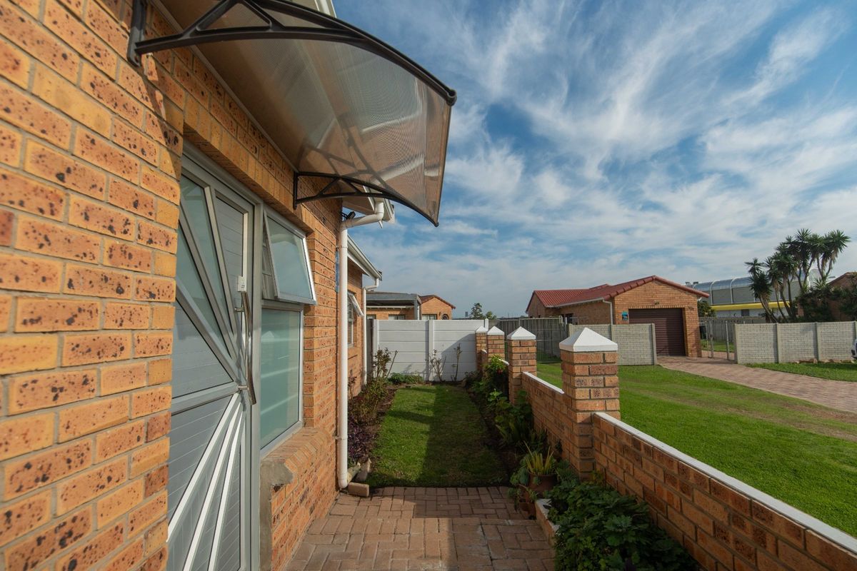 A well-maintained rear exterior view featuring a brick facade, a paved walkway, a small lawn, and a secure boundary wall.