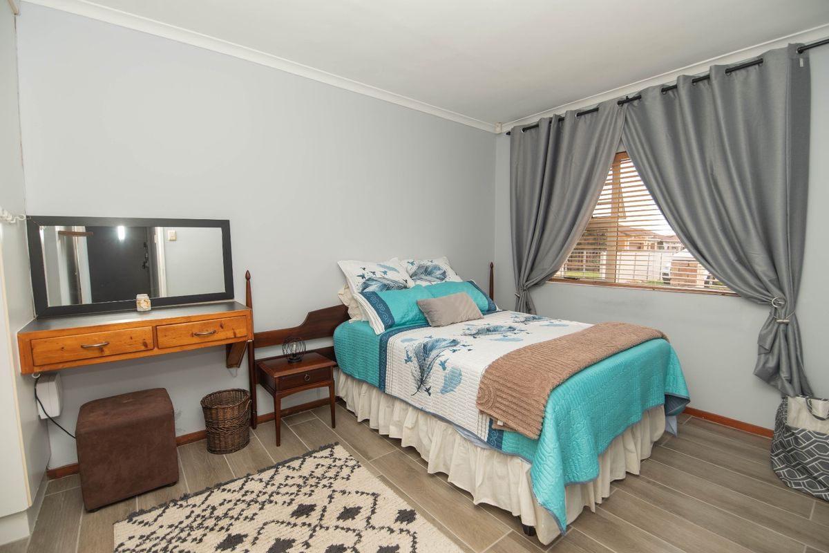 A functional bedroom featuring tiled flooring, neutral wall finishes, and window treatments including venetian blinds and curtains.