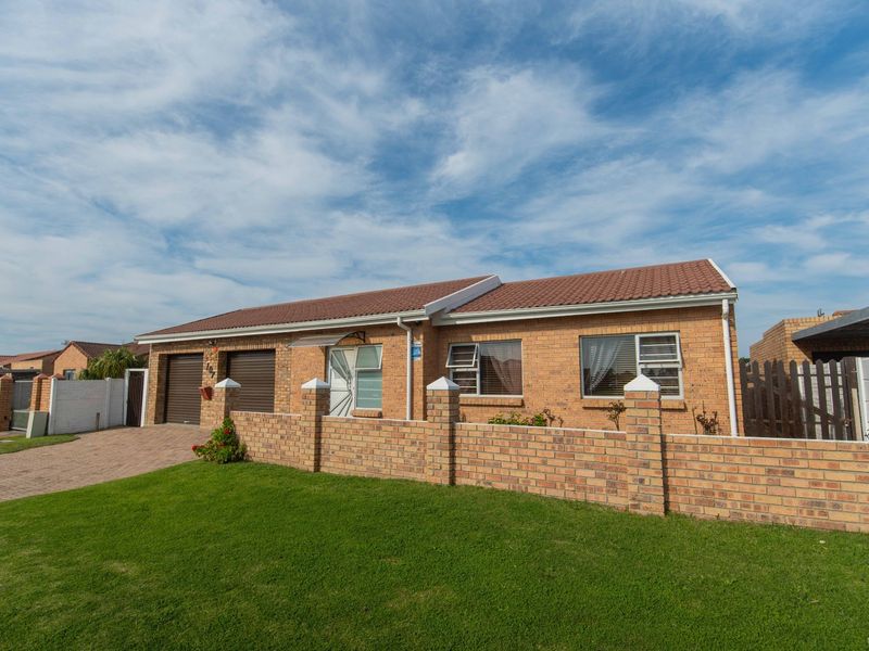 Front view of a well-maintained single-story brick house featuring a tiled roof, double garage, and a paved driveway with a brick boundary wall.