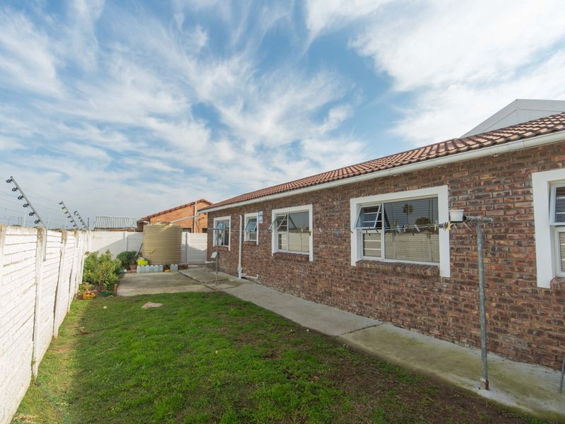 Rear view of the house featuring a face brick facade, tiled roof, aluminium windows, concrete apron, and a water storage tank in the garden.