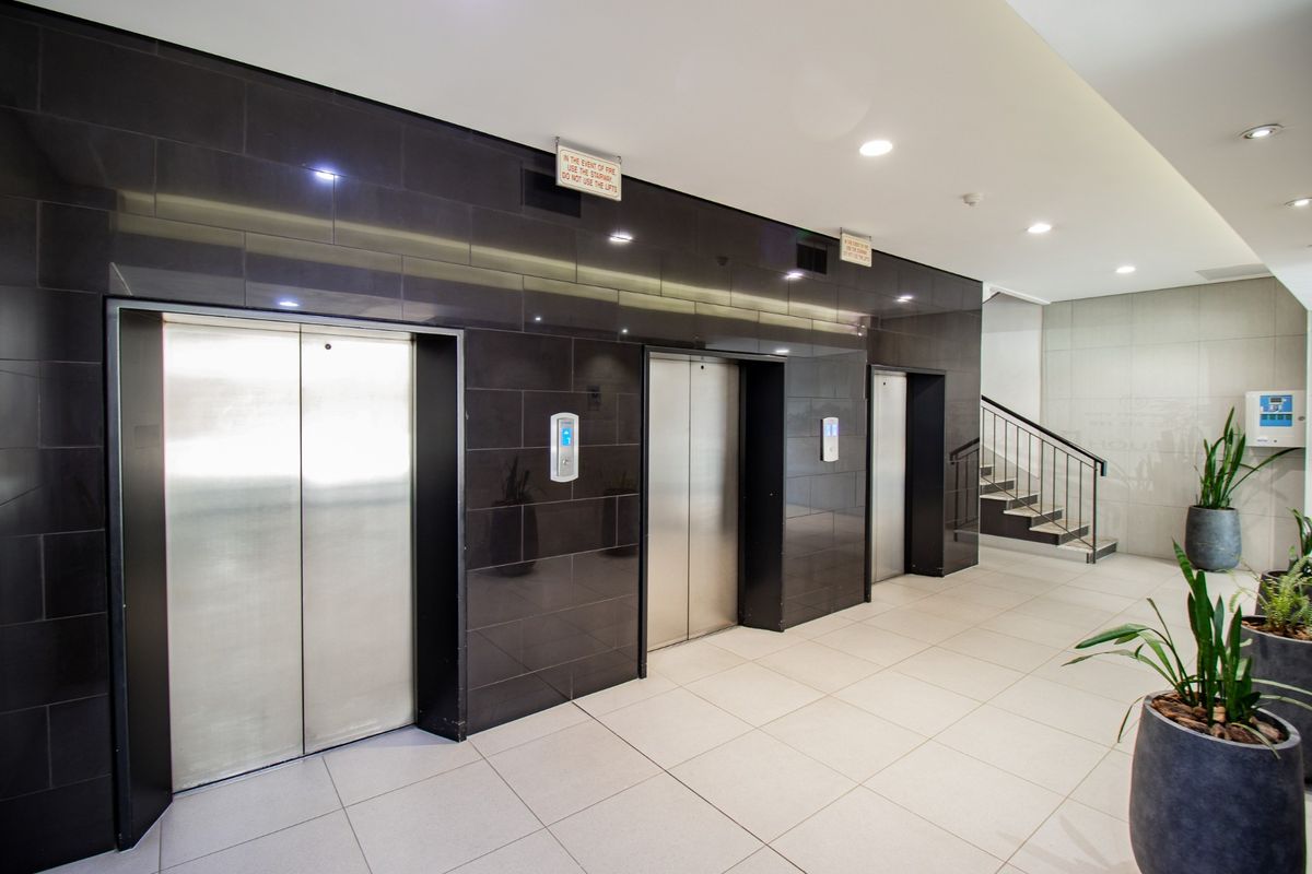 Modern commercial building lobby featuring a bank of three stainless steel elevators, black tiled feature wall, and access to a staircase.