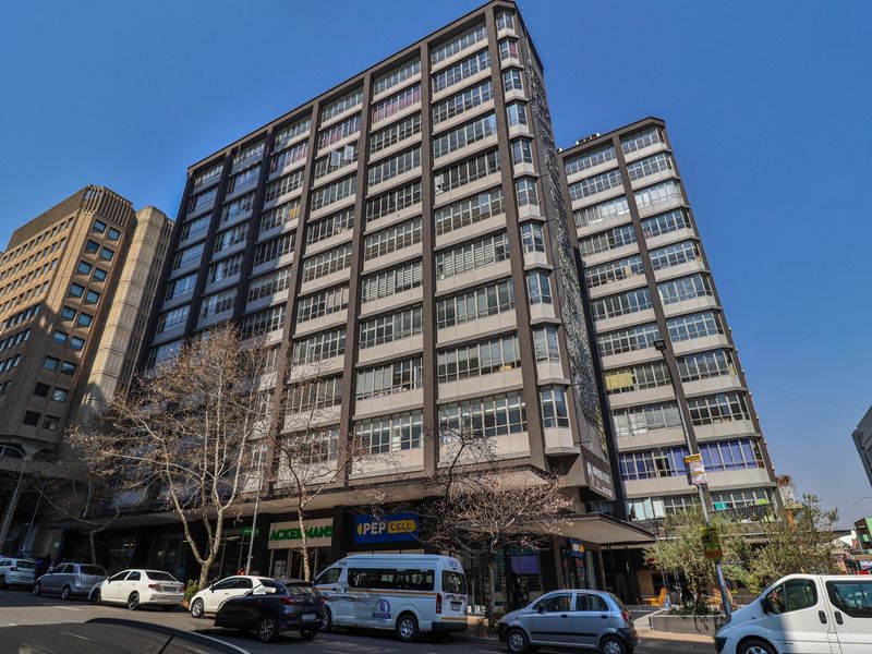 A multi-story commercial building featuring a prominent facade with extensive glass windows and ground-level retail storefronts in an urban setting.