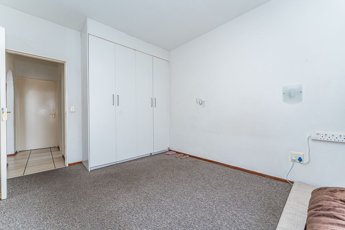 A simple, empty bedroom featuring neutral carpet flooring, white walls, and a built-in wardrobe with white cabinetry.