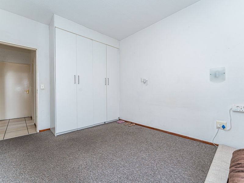 A simple, empty bedroom featuring neutral carpet flooring, white walls, and a built-in wardrobe with white cabinetry.