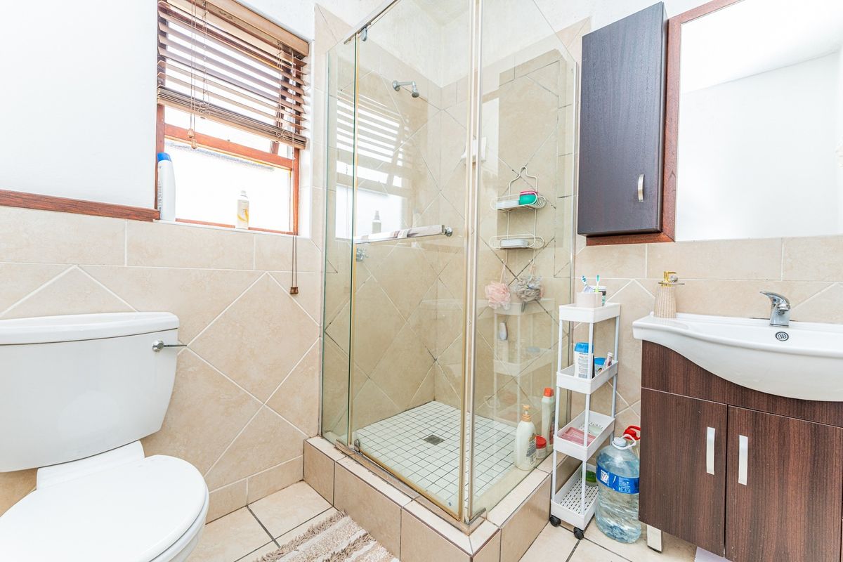 A functional bathroom featuring a glass-enclosed shower, vanity cabinet with basin, and neutral ceramic tiling throughout.