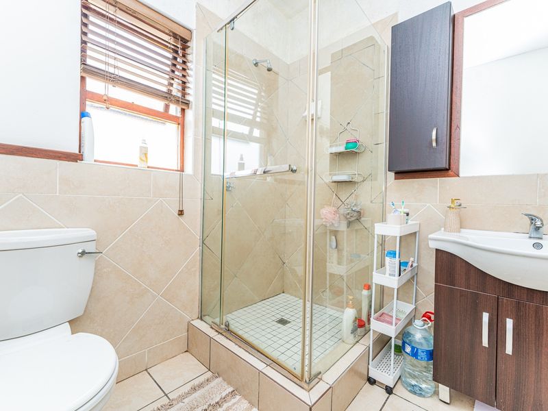 A functional bathroom featuring a glass-enclosed shower, vanity cabinet with basin, and neutral ceramic tiling throughout.