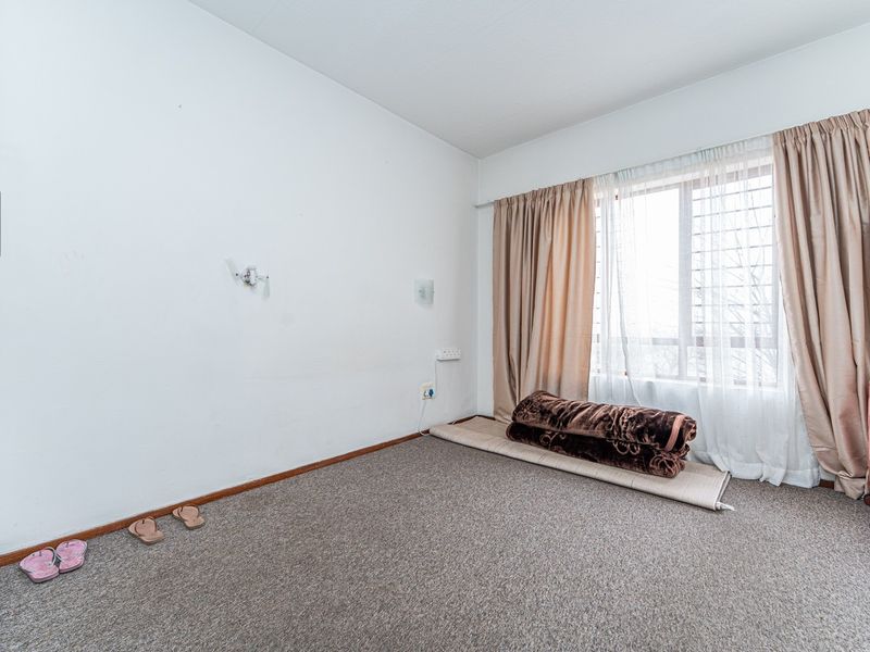 A vacant bedroom featuring carpeted flooring, a built-in cupboard, and a window fitted with security bars.