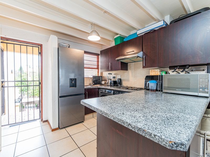 Compact kitchen featuring dark wood cabinetry, granite countertops, exposed beam ceilings, and direct access to an outdoor area via a security gate.