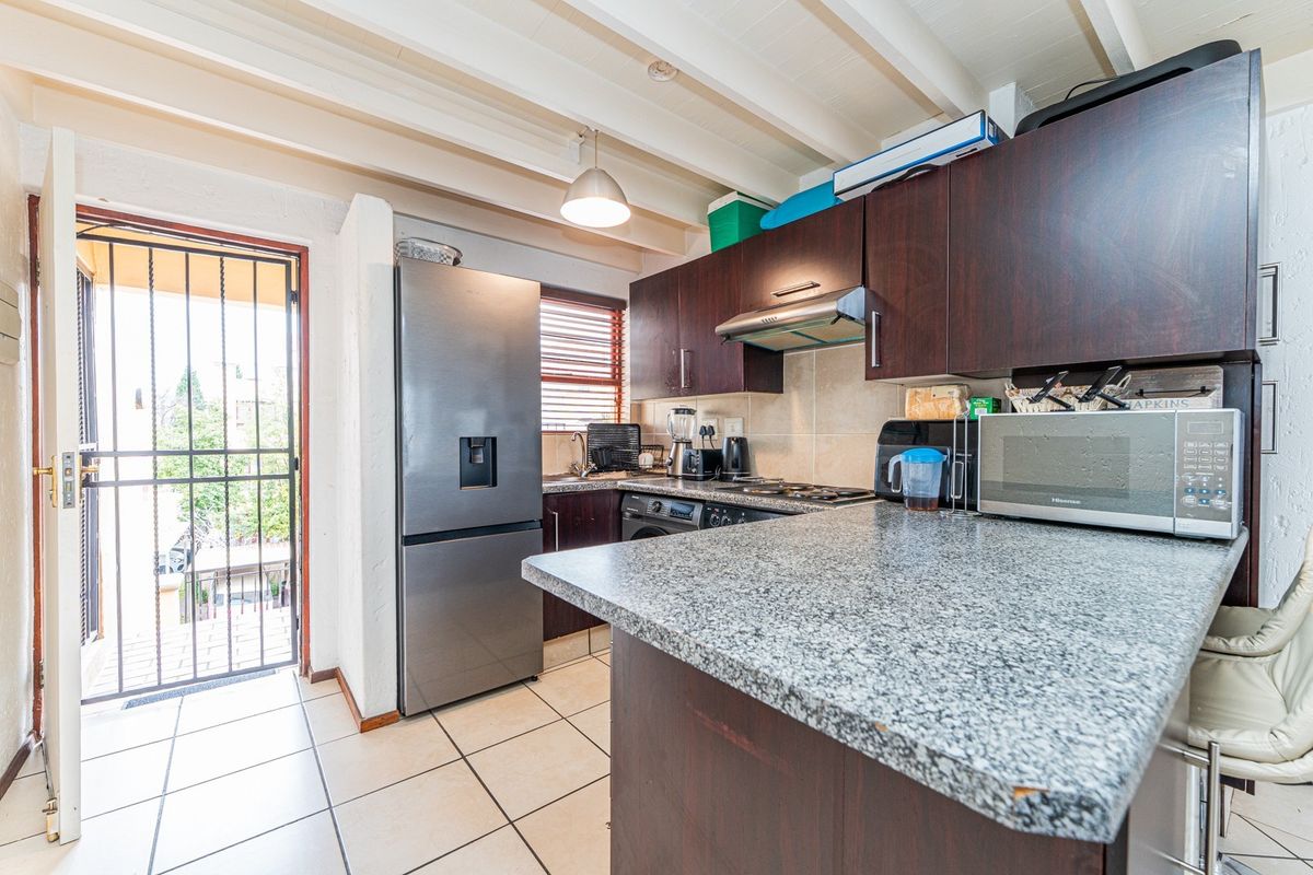 Compact kitchen featuring dark wood cabinetry, granite countertops, exposed beam ceilings, and direct access to an outdoor area via a security gate.