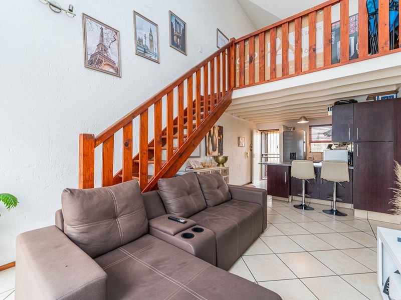 Open-plan living area featuring a timber staircase leading to a mezzanine level, tiled flooring, and a functional kitchen with dark cabinetry.