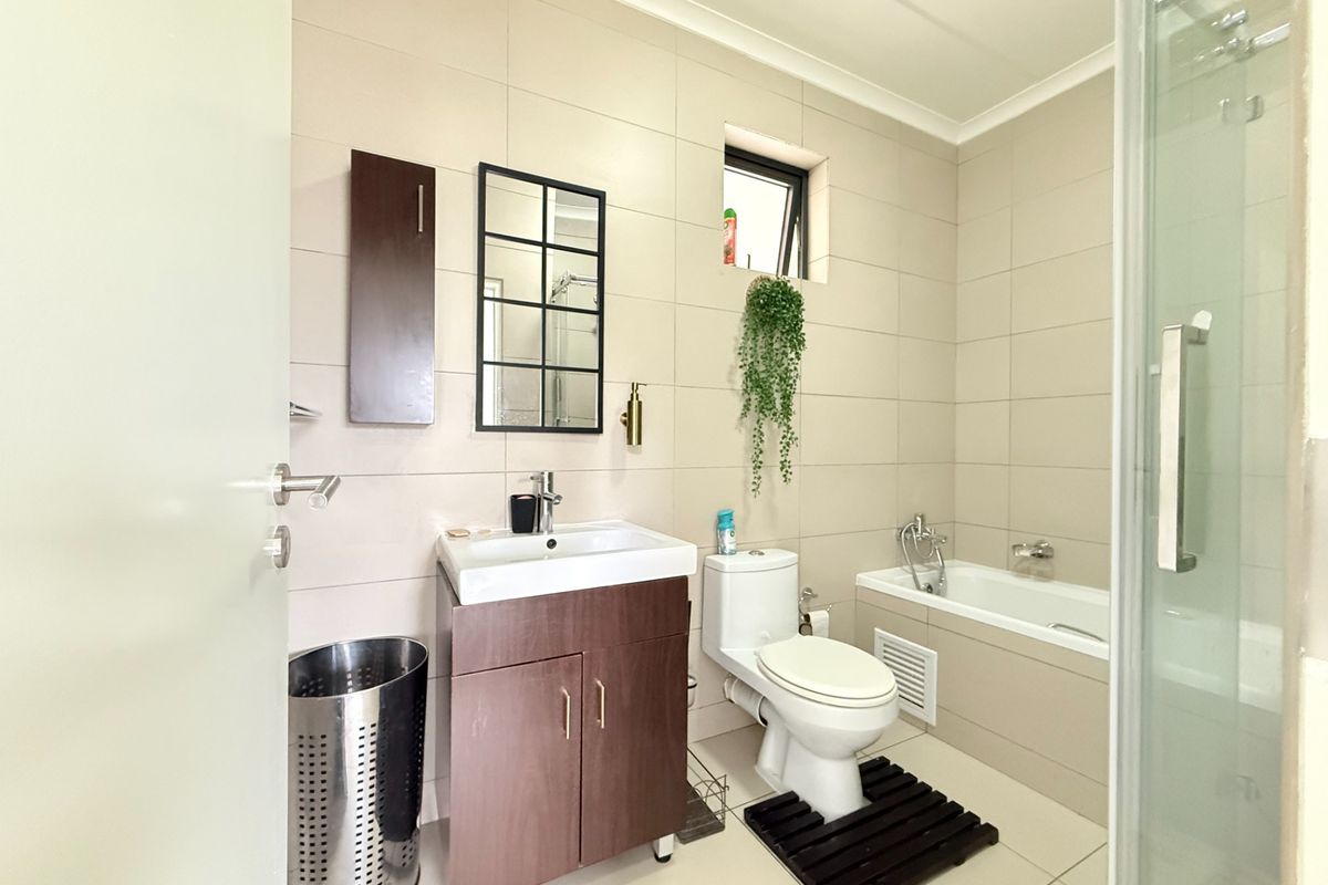 A well-maintained bathroom featuring a vanity cabinet, ceramic basin, bathtub, and a separate shower enclosure with neutral wall and floor tiling.