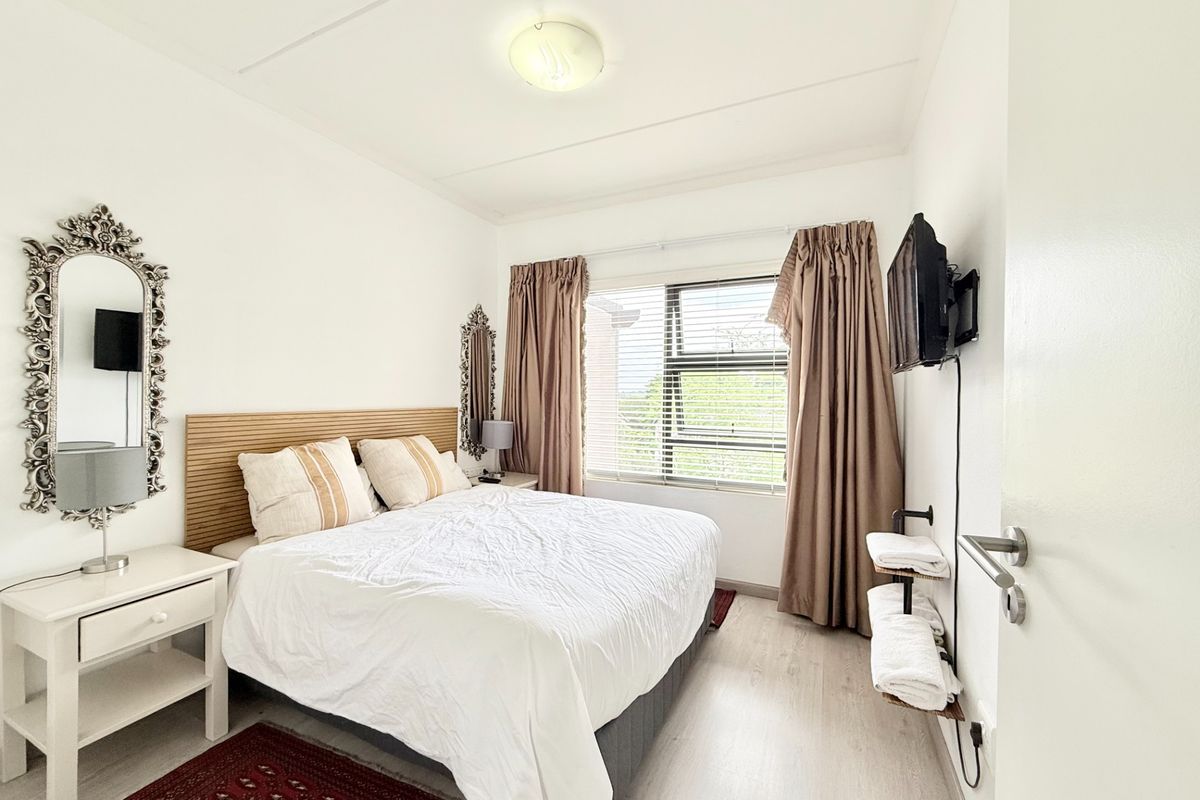 A well-maintained bedroom featuring light laminate flooring, a large window with blinds, and a wall-mounted television bracket.