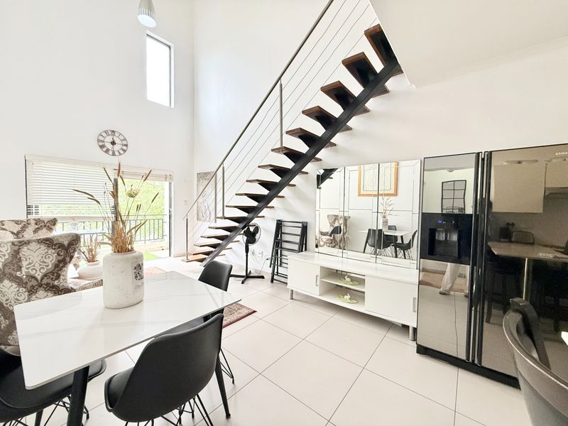Spacious open-plan living area featuring a modern floating staircase, double volume ceilings, and large sliding doors leading to a balcony.