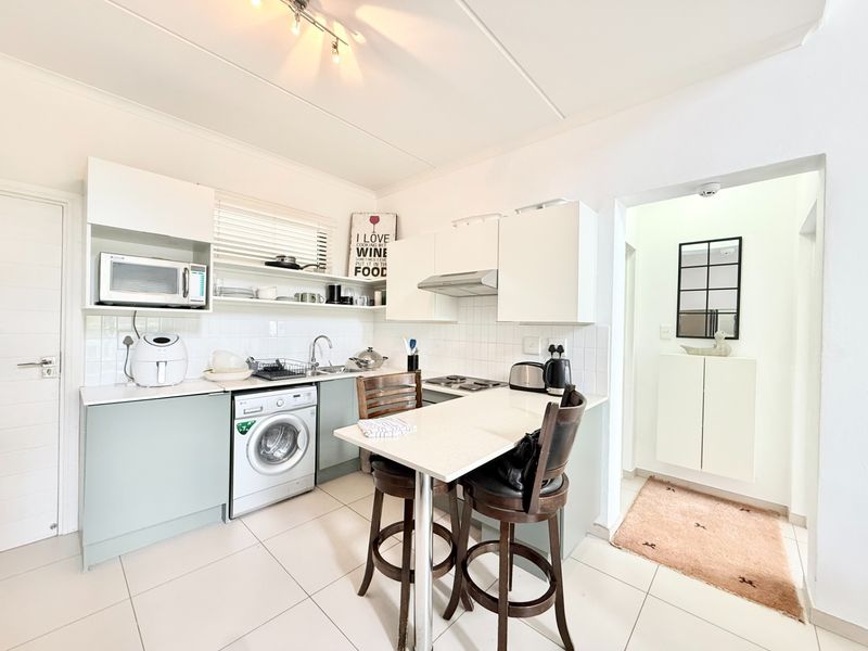 Compact kitchen featuring white cabinetry, tiled backsplash, integrated hob, extractor fan, and dedicated space for a washing machine with tiled flooring throughout.