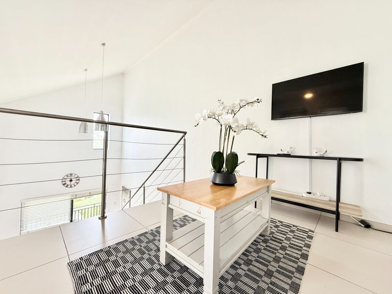 A bright living area featuring vaulted ceilings, modern tiled flooring, and a sleek stainless steel cable railing overlooking the lower level.