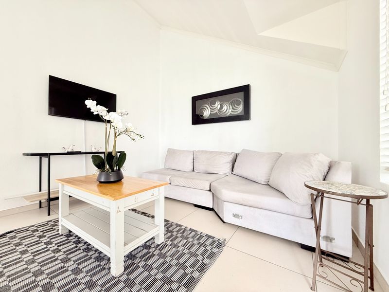 A bright living room featuring neutral tiled flooring and a distinctive sloped ceiling, creating an open and airy atmosphere.