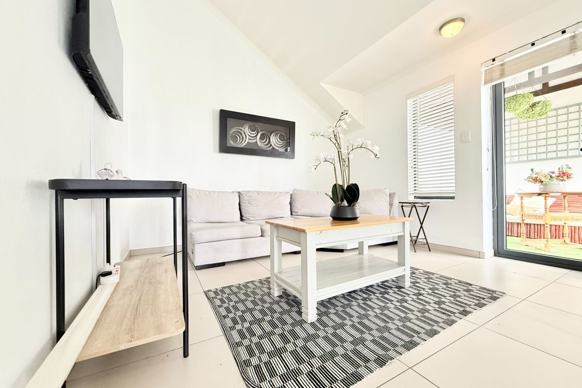 A bright living room featuring tiled flooring, a sloped ceiling, and a sliding glass door providing access to an outdoor patio area.