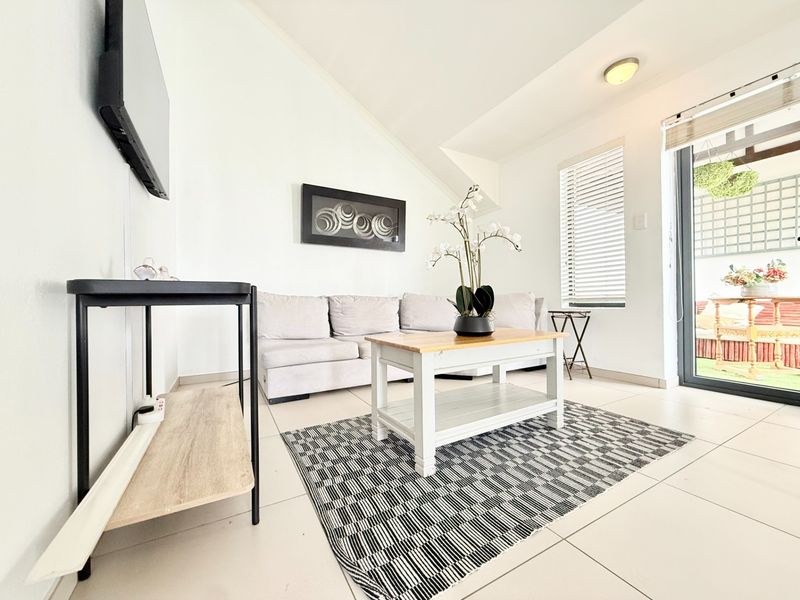 A bright living room featuring tiled flooring, a sloped ceiling, and a sliding glass door providing access to an outdoor patio area.
